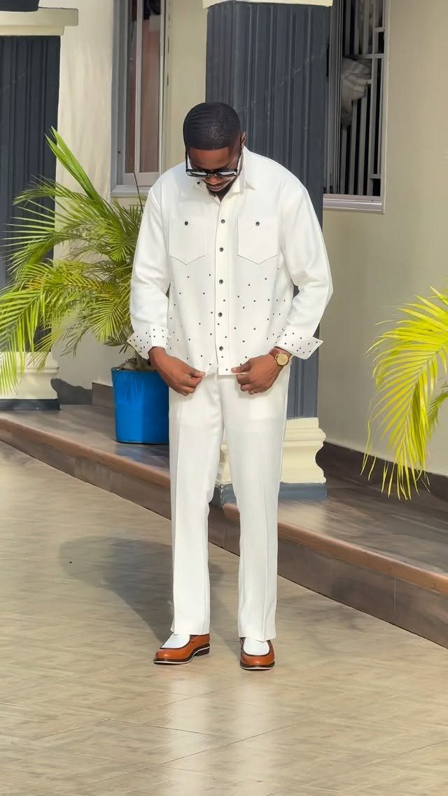 Man wearing a white jacket and white trousers with brown loafers outdoors.