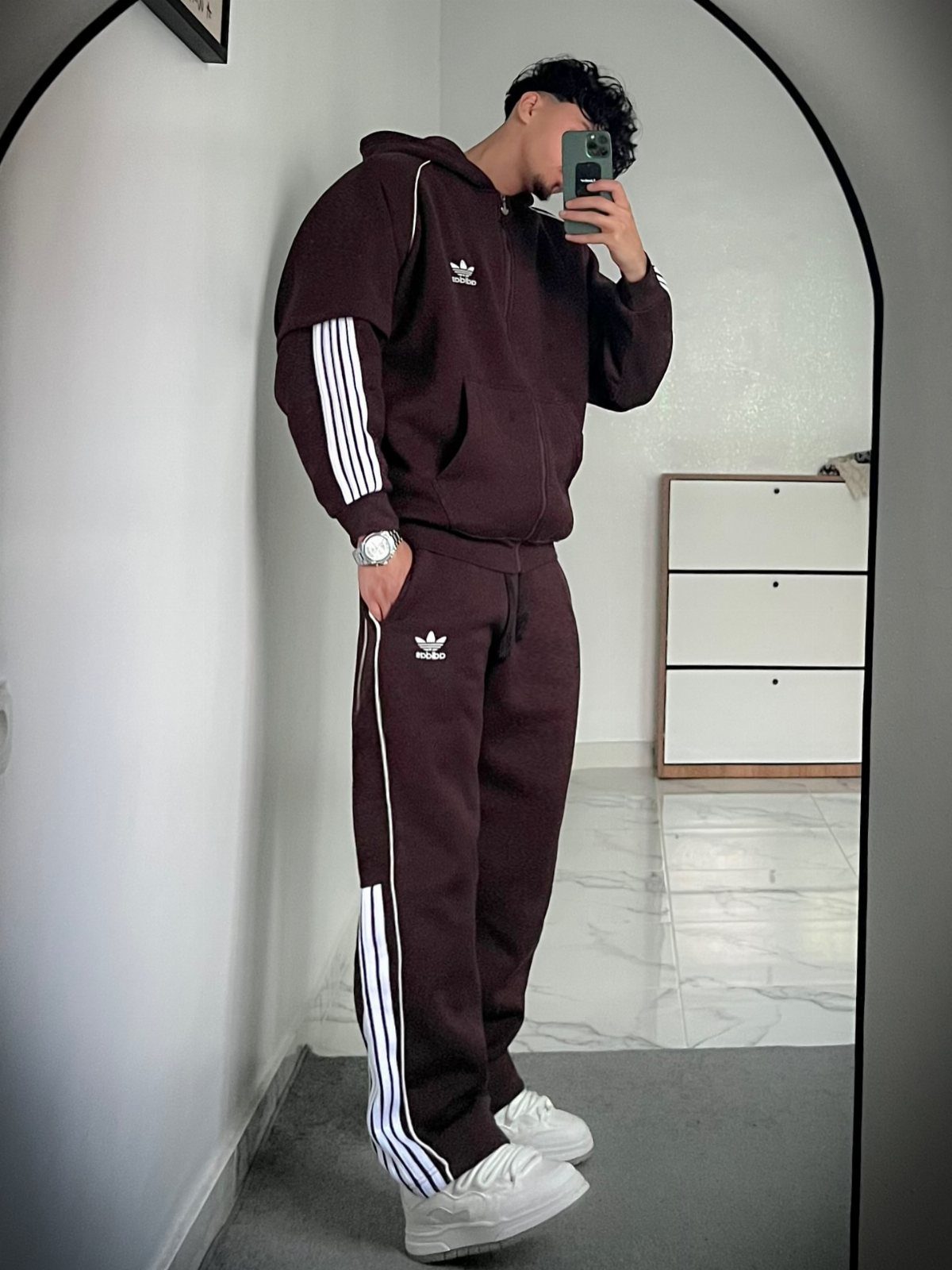 Man wearing a maroon Adidas zip-up hoodie and matching track pants with white sneakers.