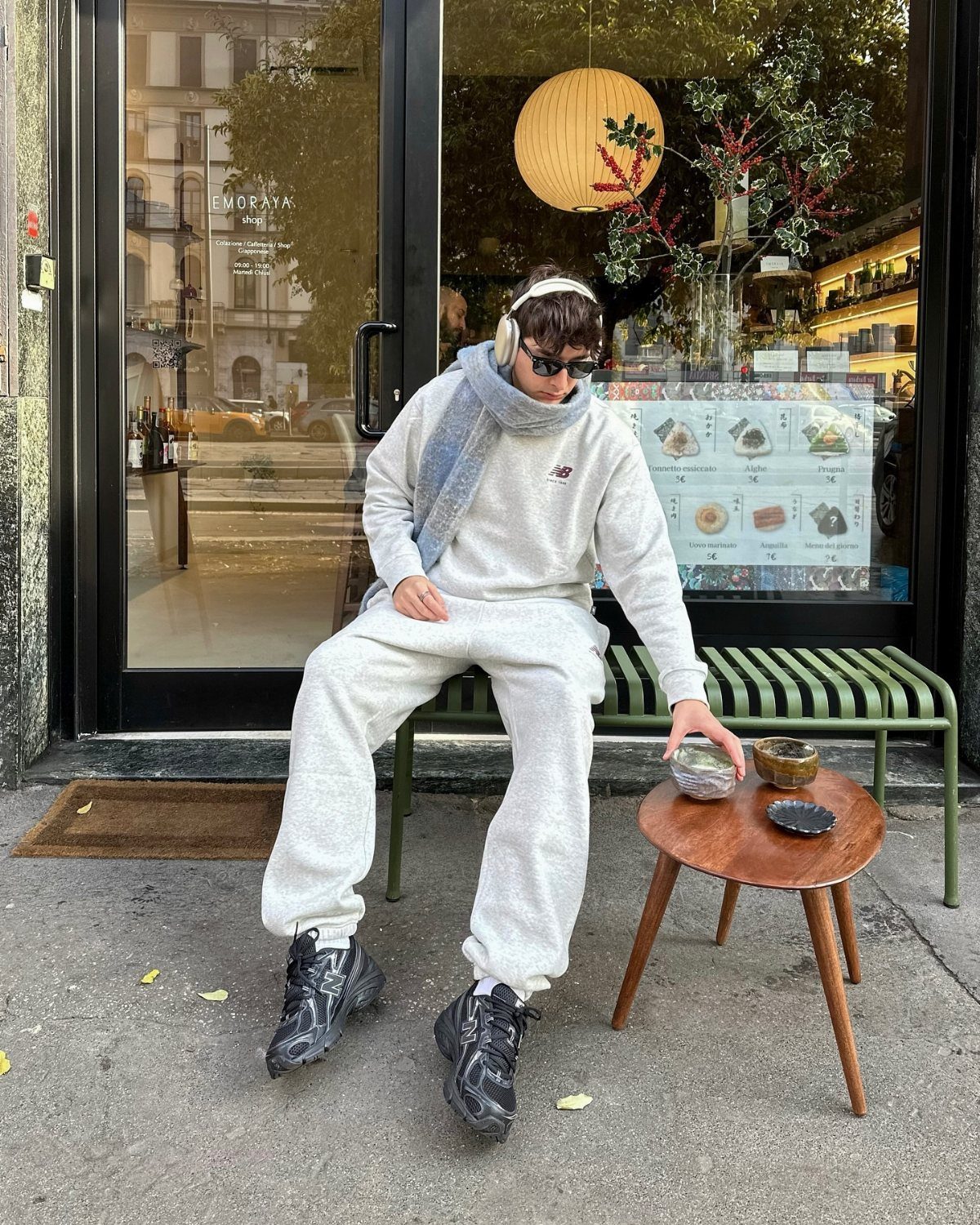 Man in grey athleisure outfit and black sneakers sitting on a green bench.