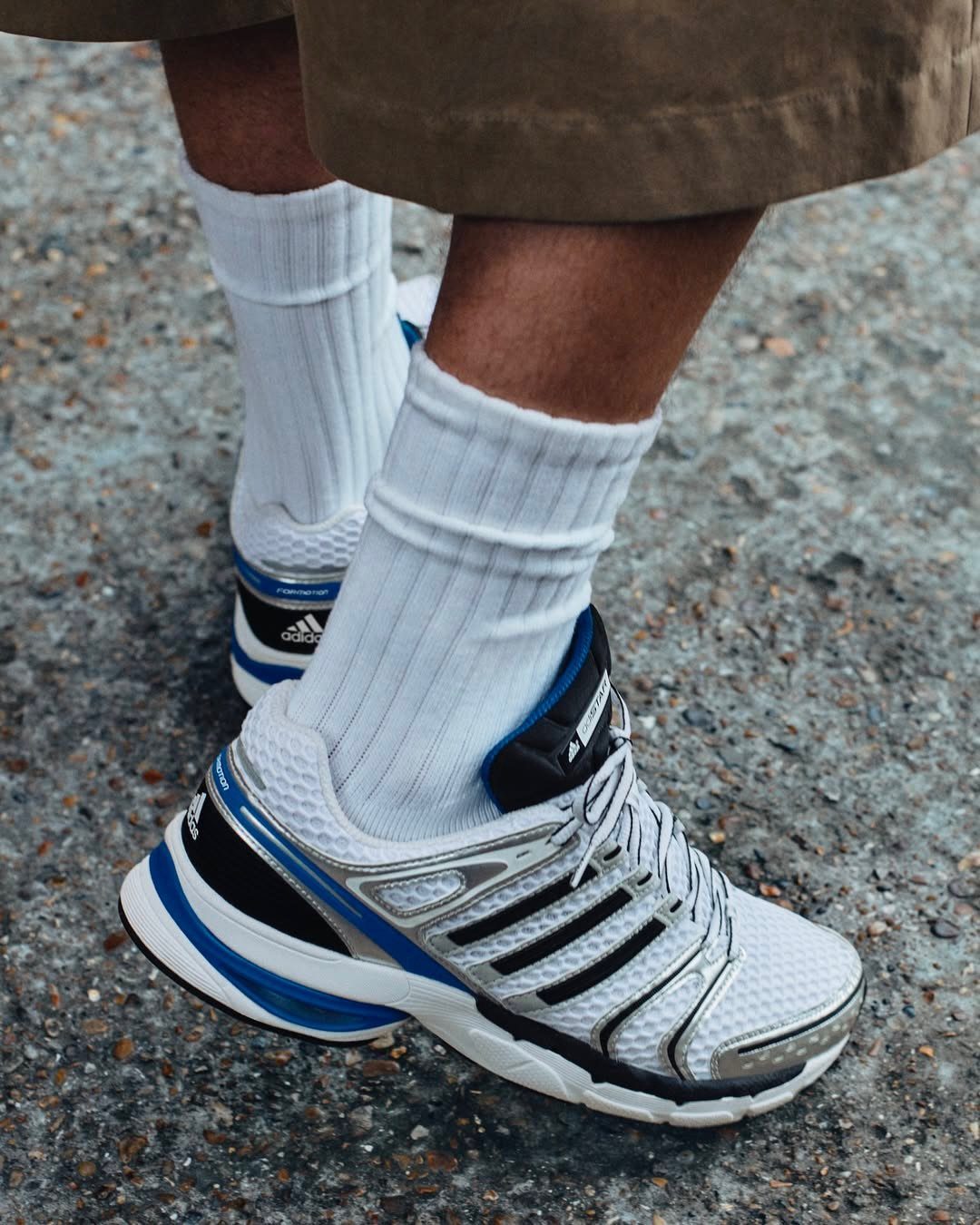 White and blue retro running shoes with white ribbed socks on asphalt.