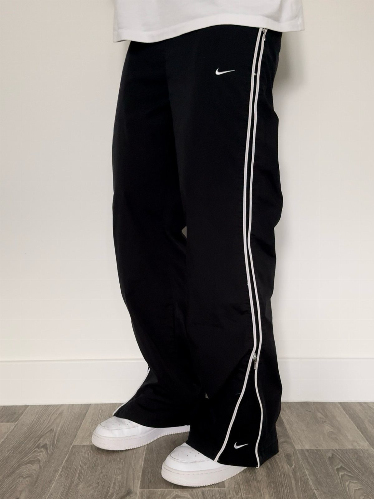 Black Nike athletic trousers with white side stripes and white sneakers.