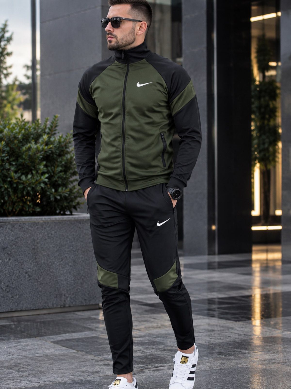 Man wearing a green and black track jacket with matching athletic pants and sneakers.
