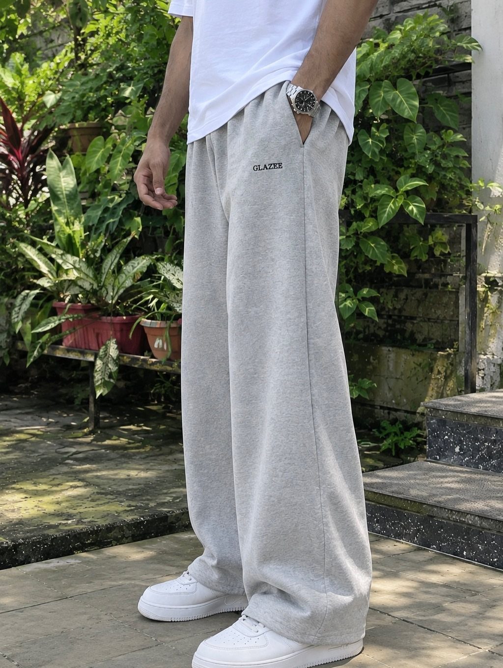 Man wearing wide-leg light grey sweatpants and white sneakers in a garden.