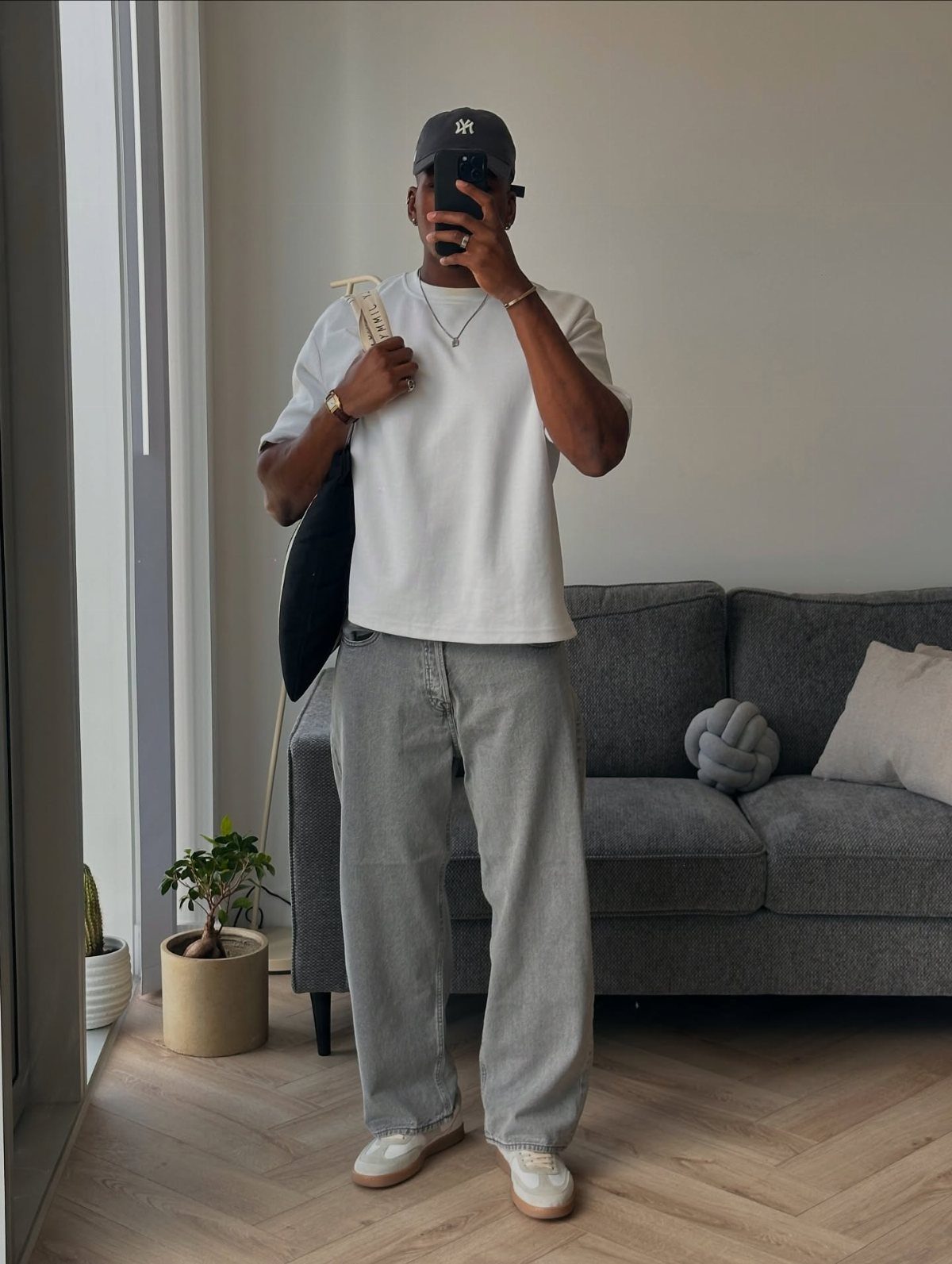 Man wearing a basic white tee, grey wide-leg pants, and a baseball cap.