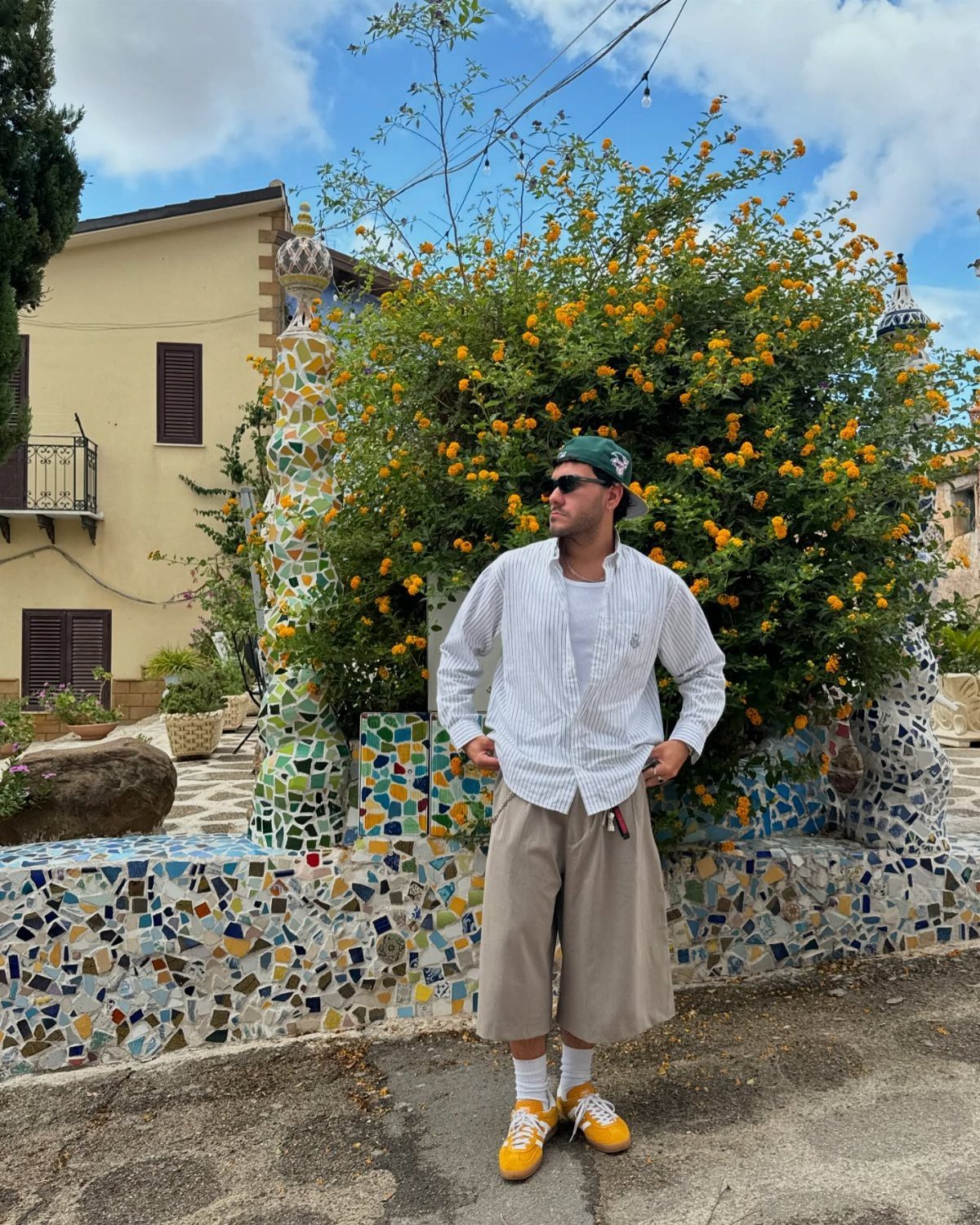 Man in white striped shirt and beige bermuda shorts posing by mosaic wall