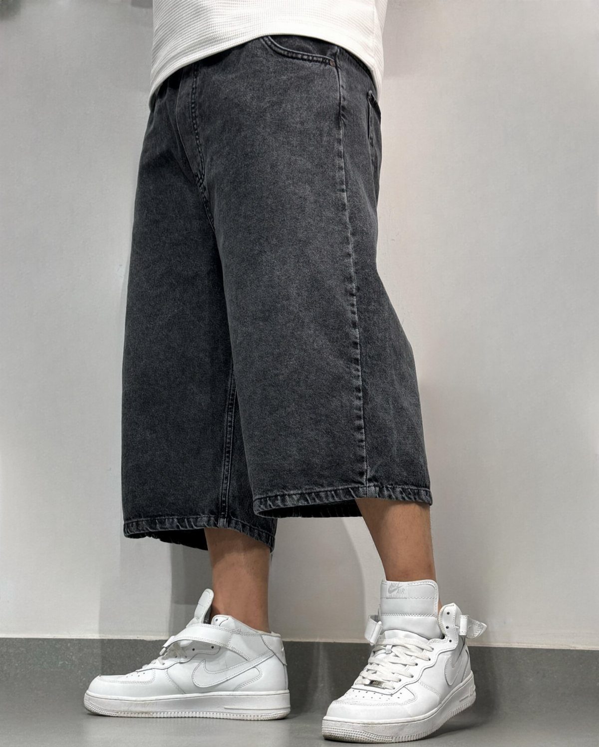 Wide-leg dark grey denim bermuda shorts paired with white sneakers and white shirt.