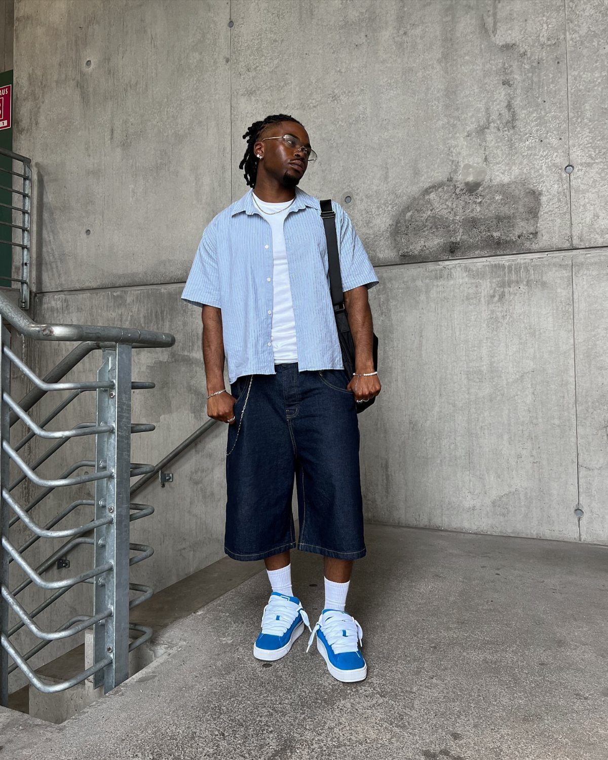 Man in light blue striped shirt and dark denim bermuda shorts with sneakers.