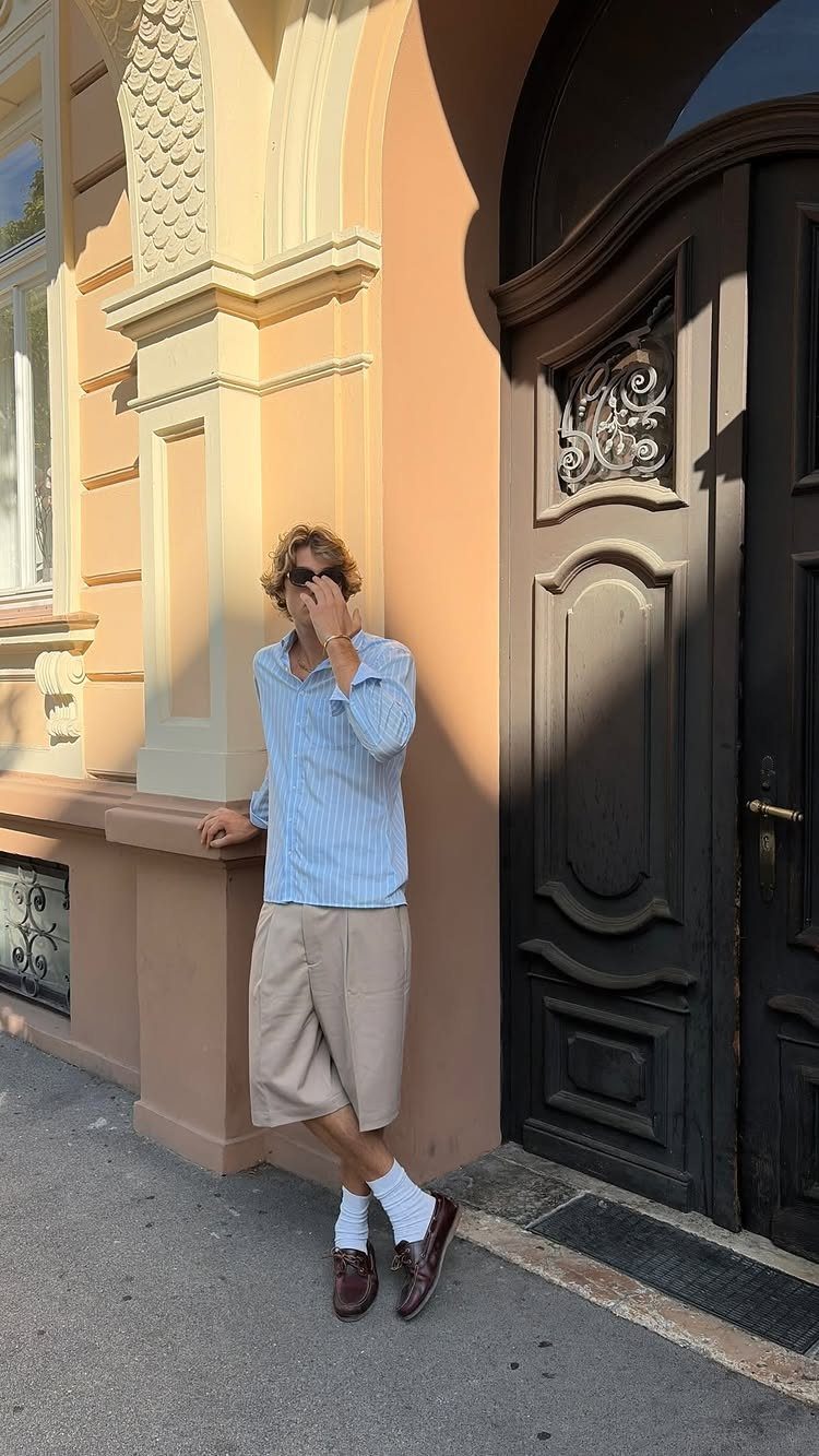 Man wearing light blue striped shirt and beige bermuda shorts standing by a door
