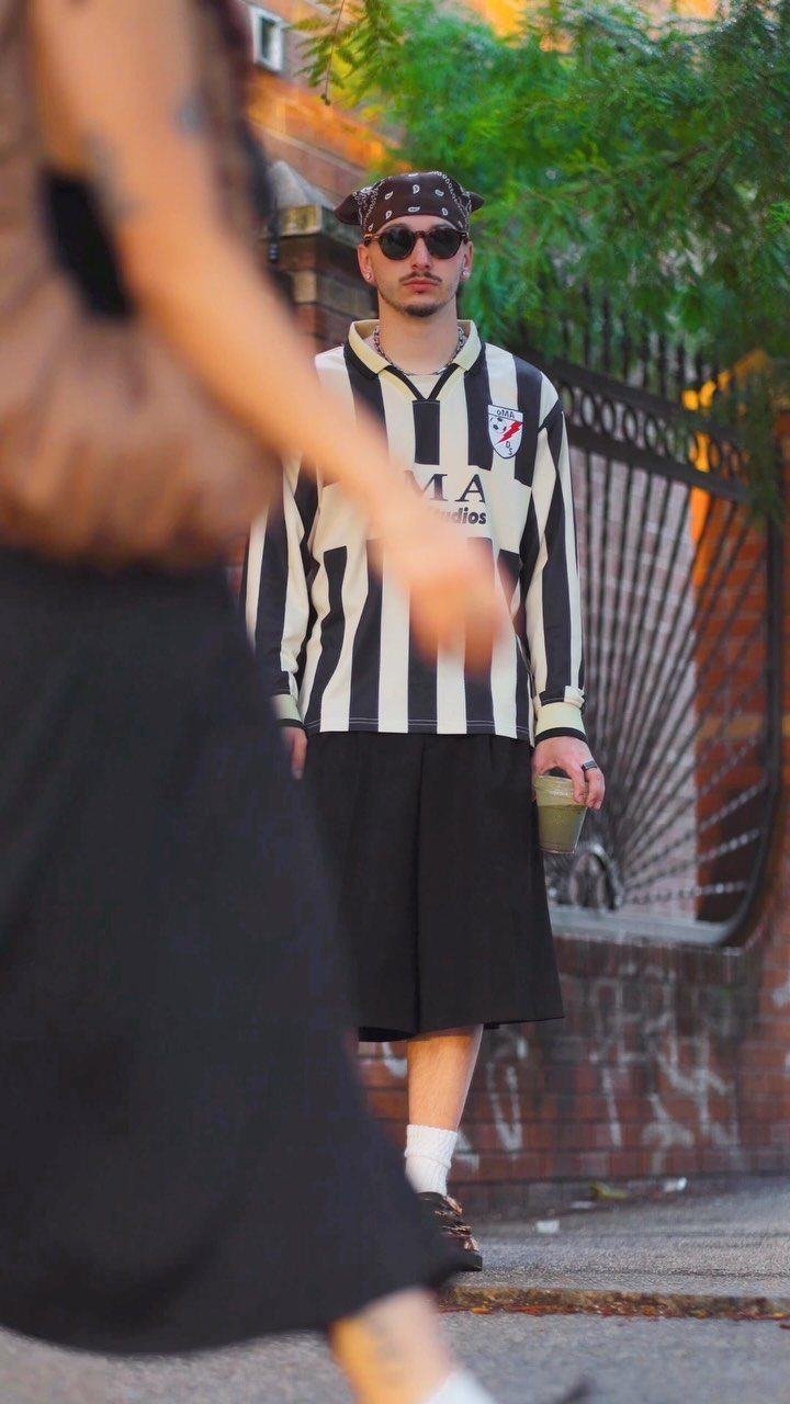 Man wearing striped jersey and wide black knee-length shorts standing on a sidewalk