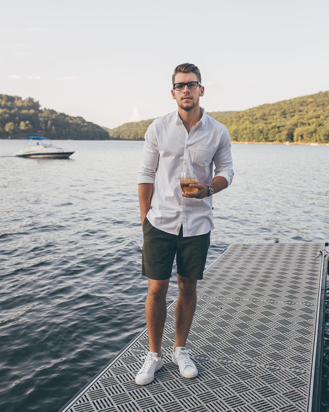 Man in white shirt and green bermuda shorts standing on a lakeside dock