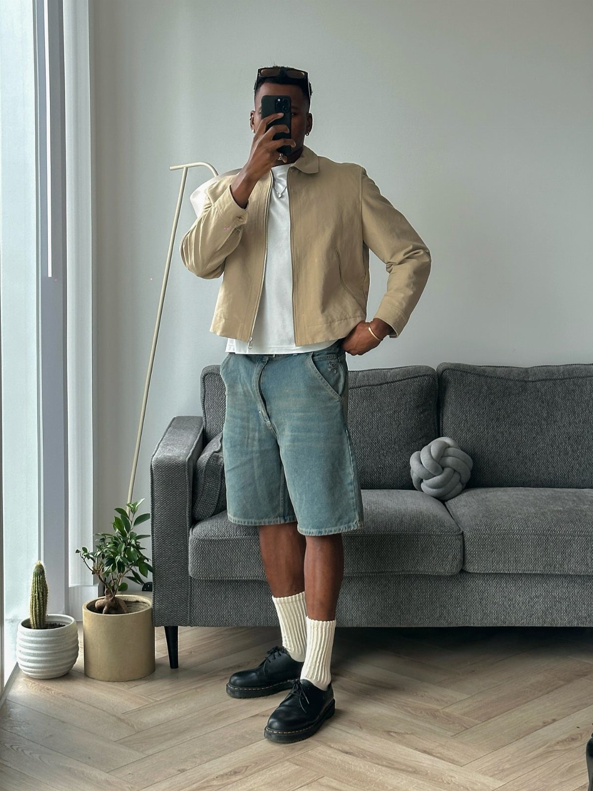 Man wearing beige jacket, denim bermuda shorts, white socks, and black leather shoes.