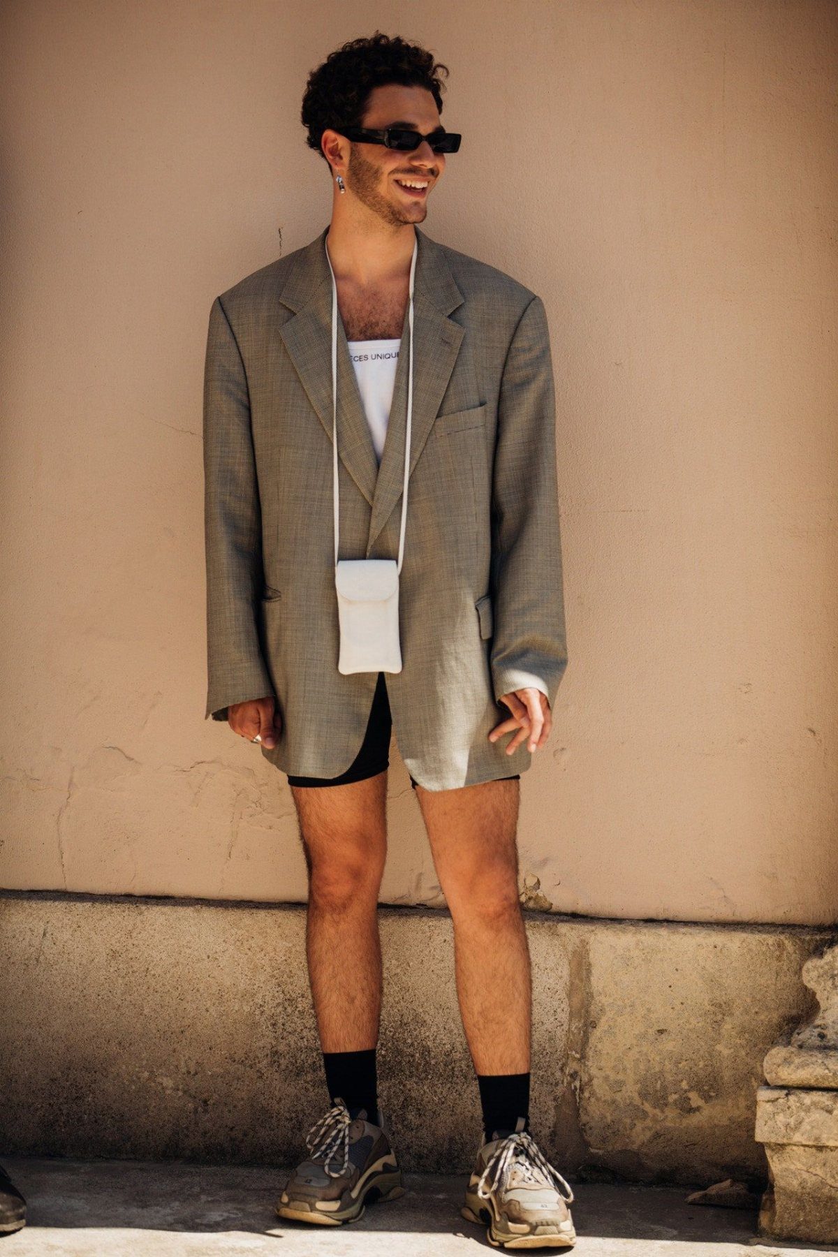 Man wearing a grey oversized blazer with black bike shorts and chunky sneakers.