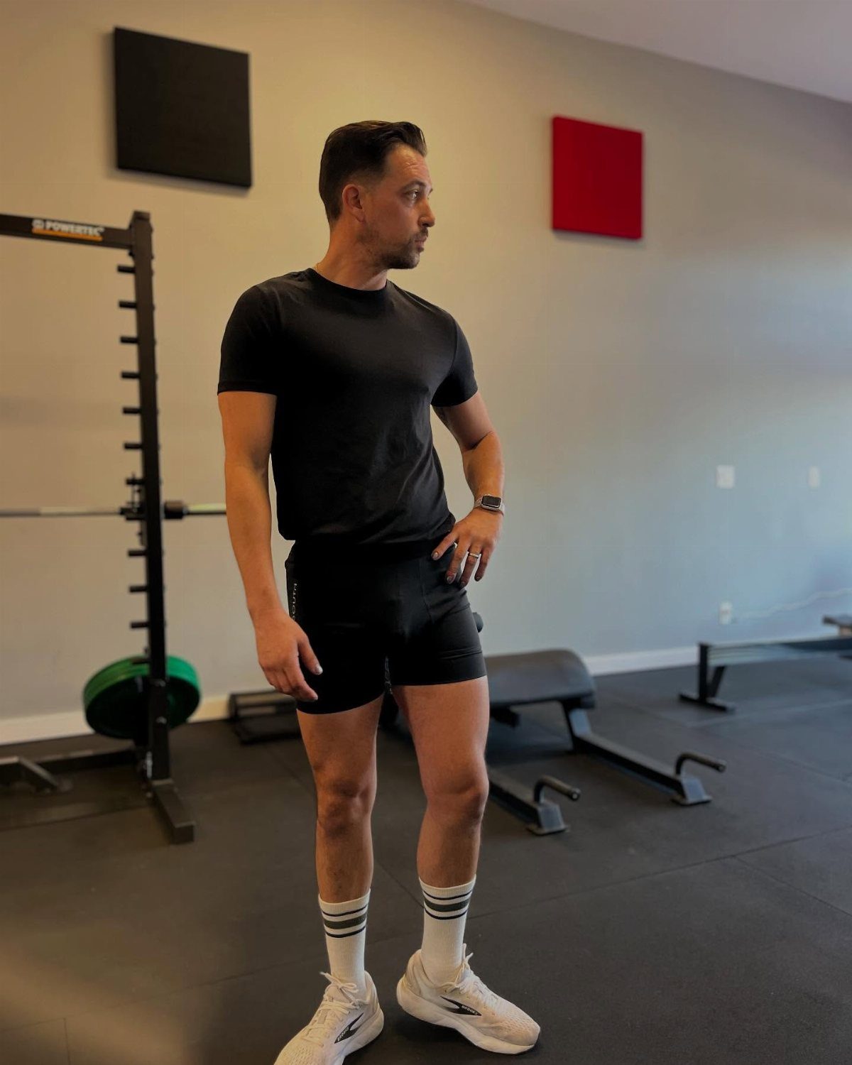 Man in black biker shorts and t-shirt posing in a gym setting