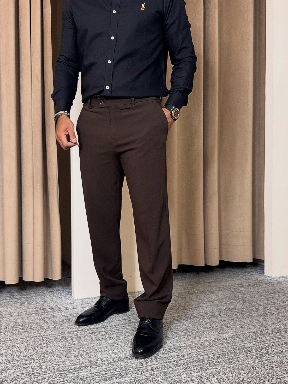 Man wearing a black button-down shirt, brown trousers, and black leather dress shoes.