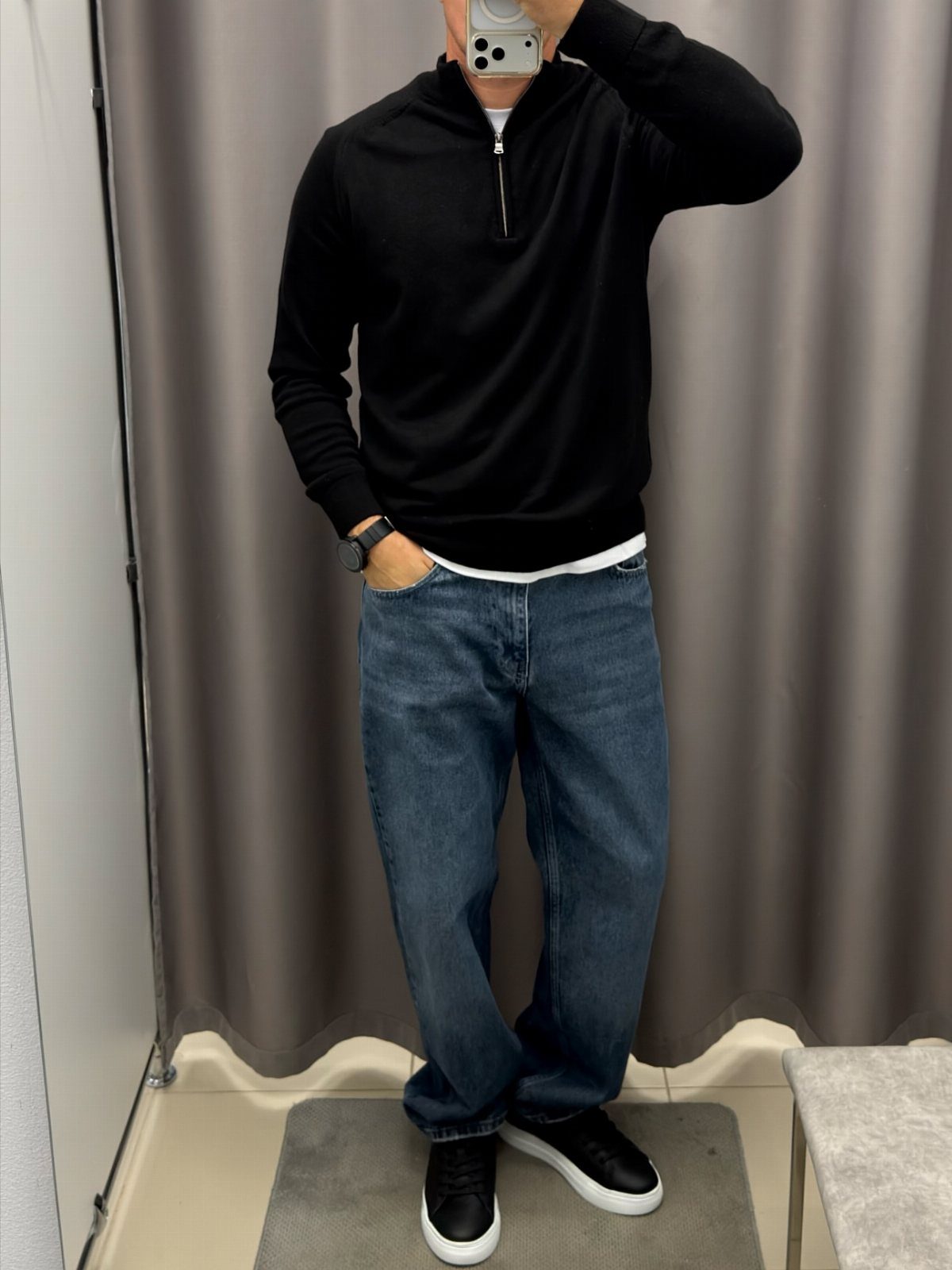 Person wearing a black quarter-zip sweater and blue jeans with black sneakers.