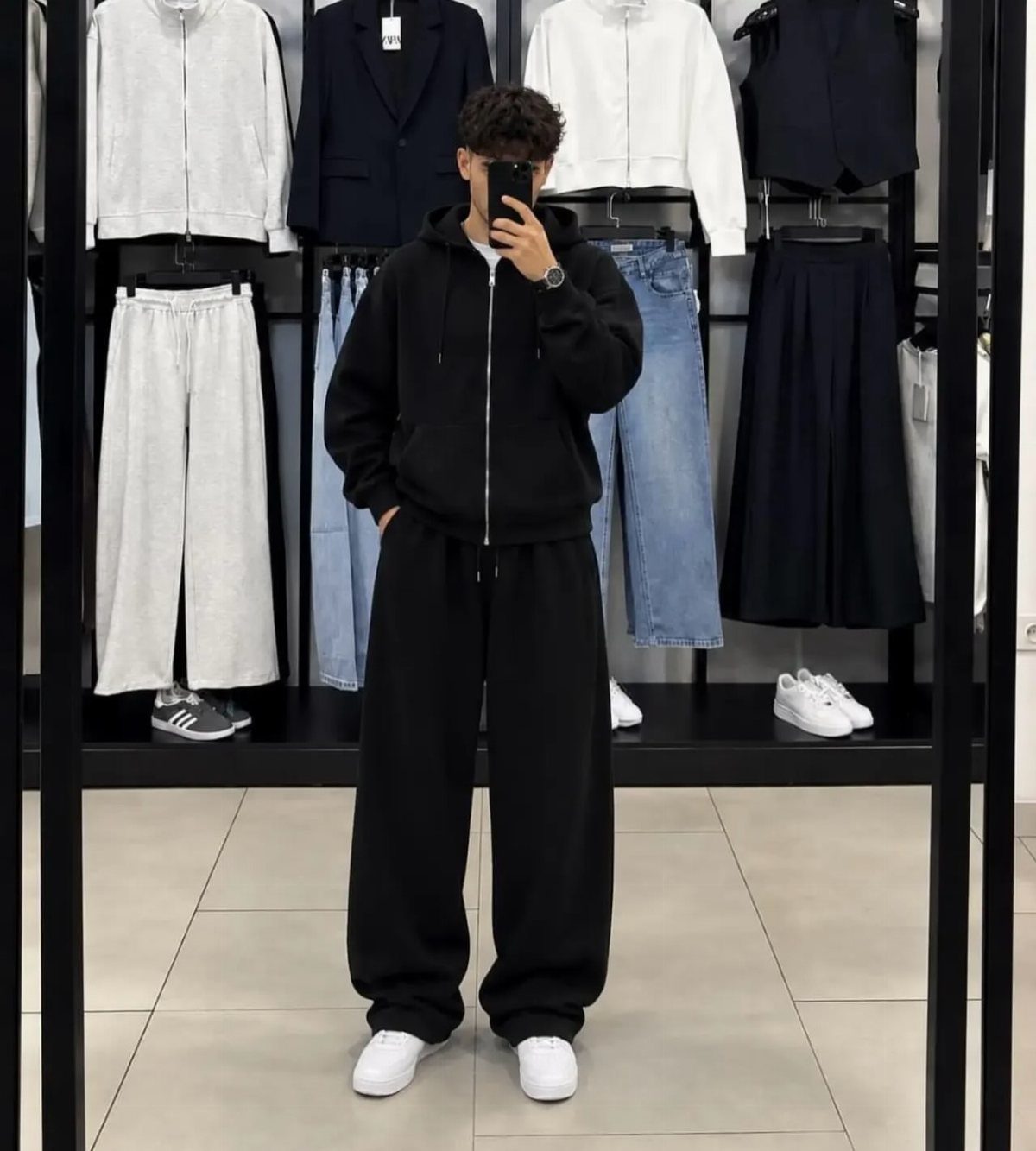 Person wearing a black hooded sweater and matching black sweatpants with white sneakers.