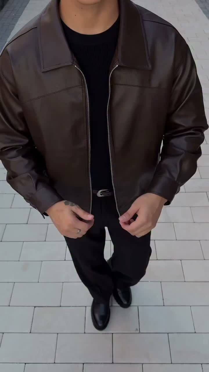 Person wearing a brown leather jacket over a black sweater and black trousers.