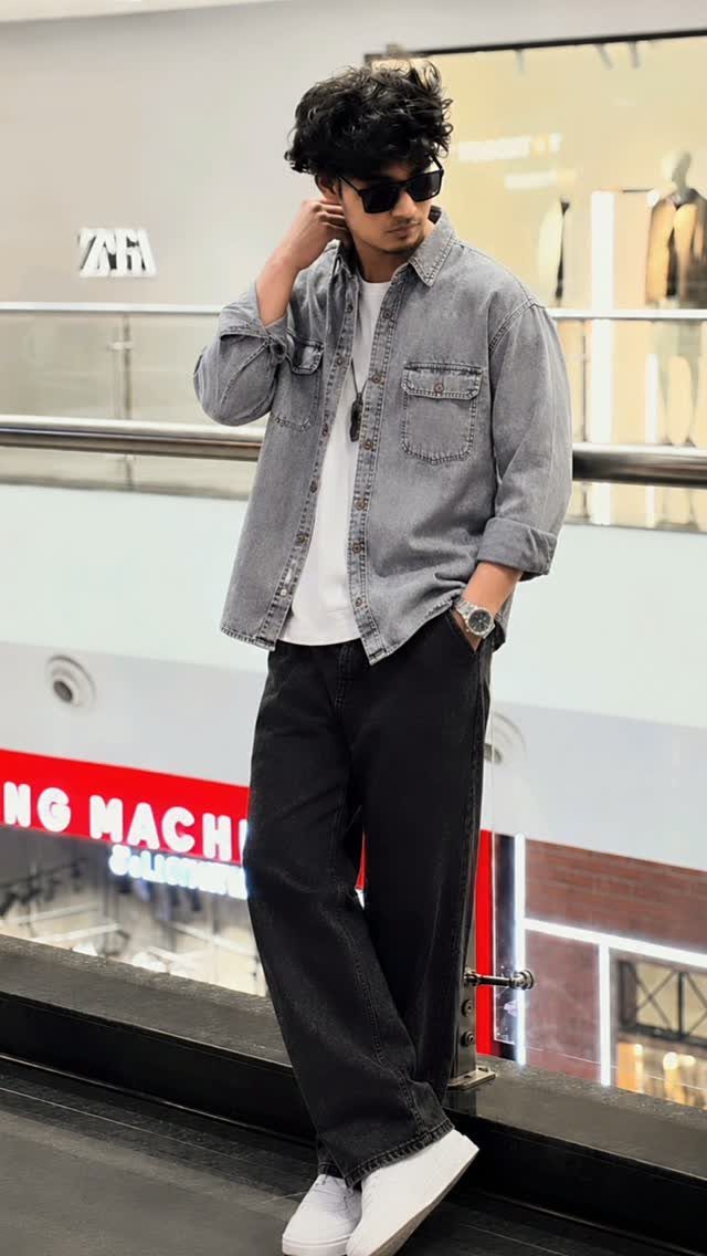 Man wearing a light blue denim shirt, white t-shirt, and wide black trousers.