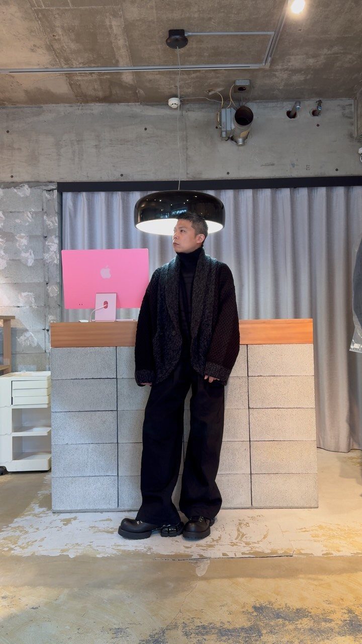 Person wearing a chunky black knit cardigan and wide-leg black trousers in a studio