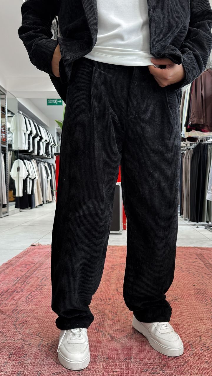 Person wearing black corduroy trousers, a black jacket, white t-shirt, and white sneakers.
