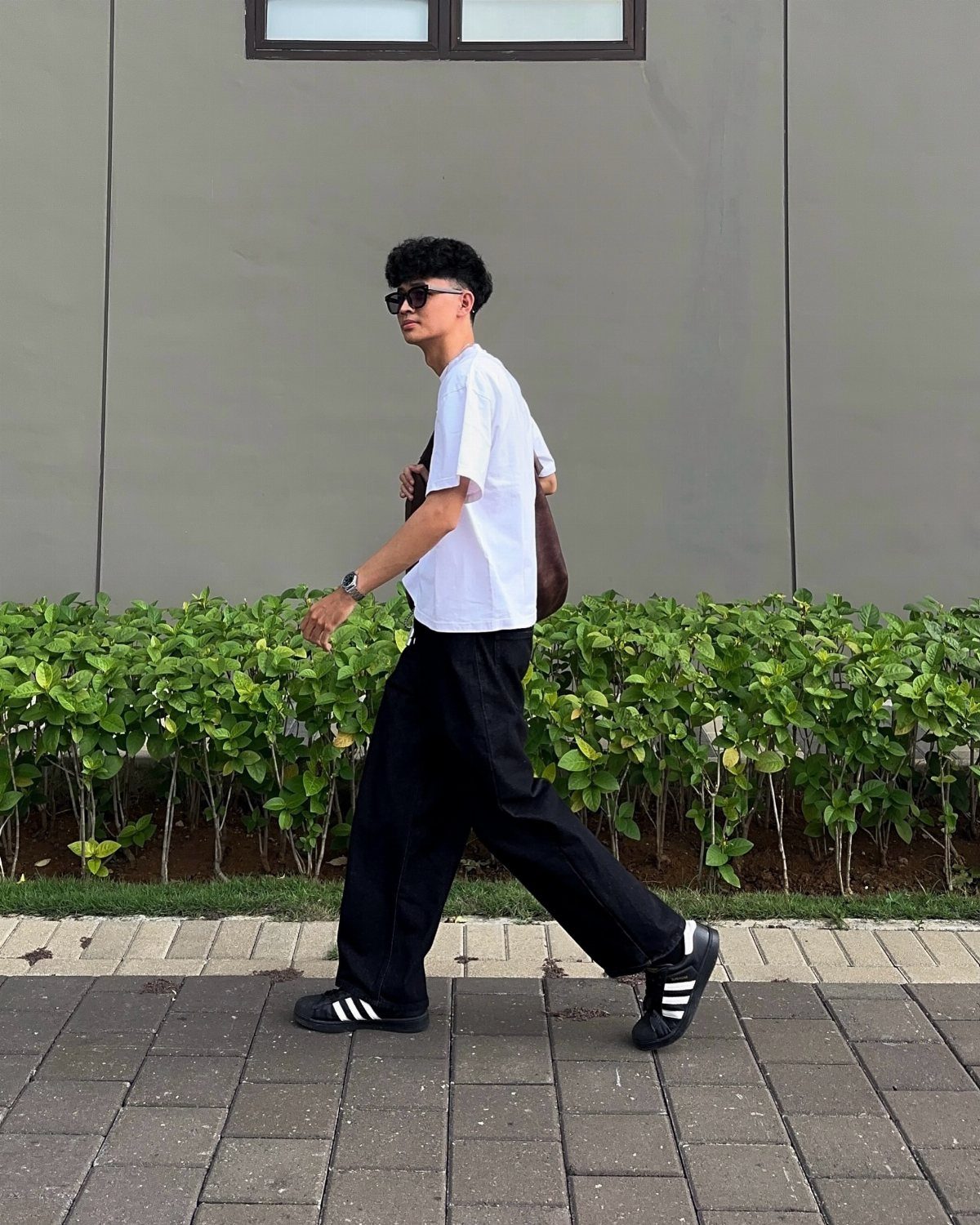 Man wearing a white t-shirt and wide black trousers walking on a paved path.