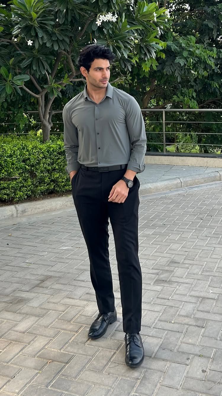 Man wearing a grey button-down shirt and black formal trousers on a paved path.