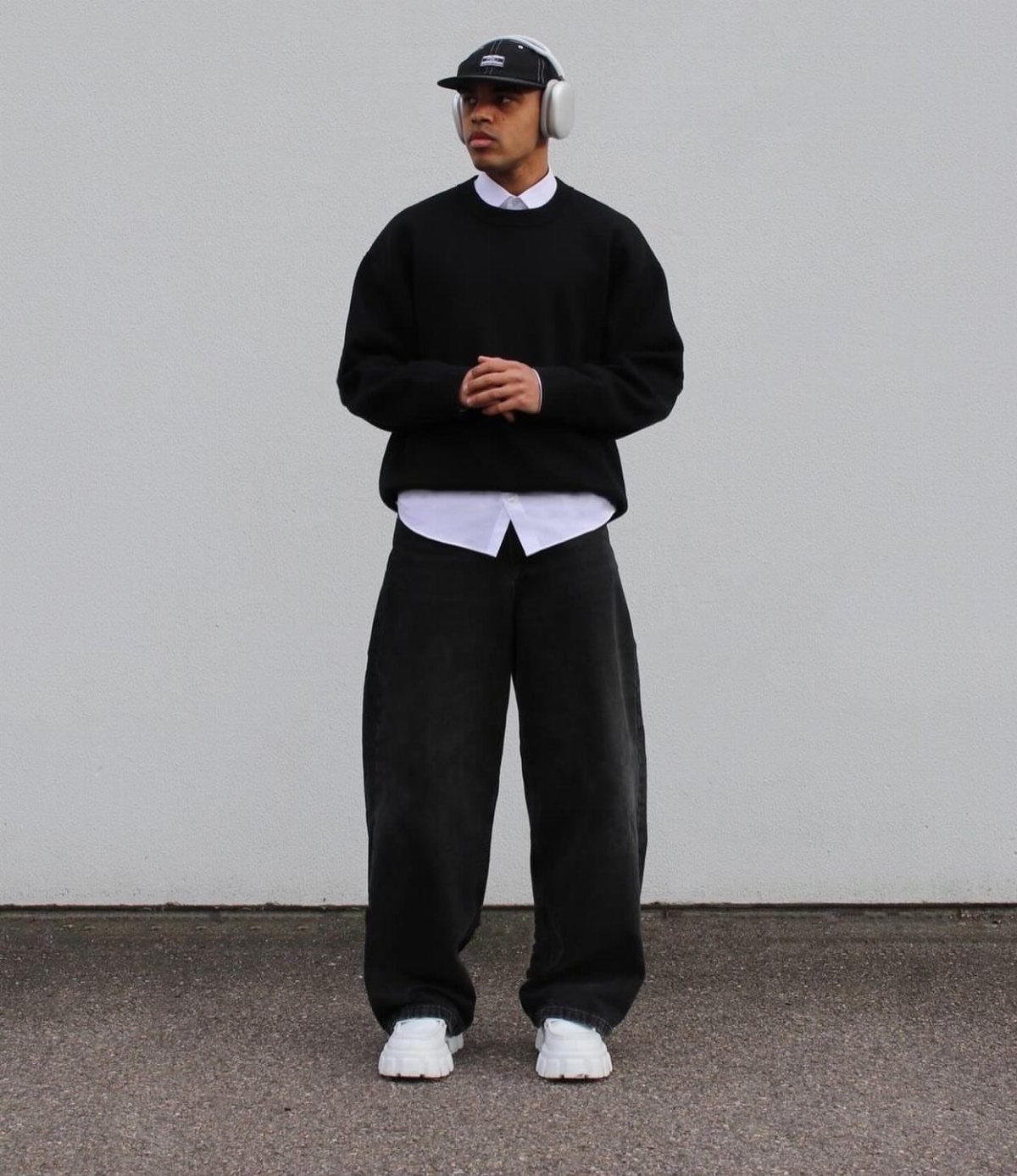 Man wearing wide-leg black trousers, black sweater, white shirt, and white sneakers.