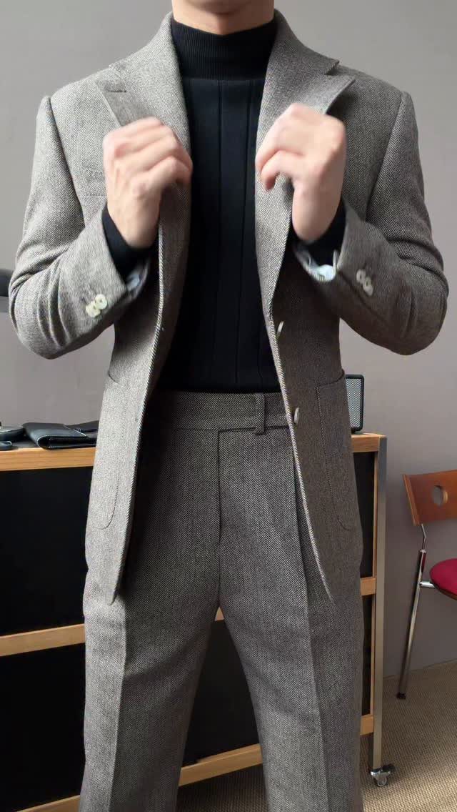 Person wearing a black turtleneck under a grey herringbone tailored suit.