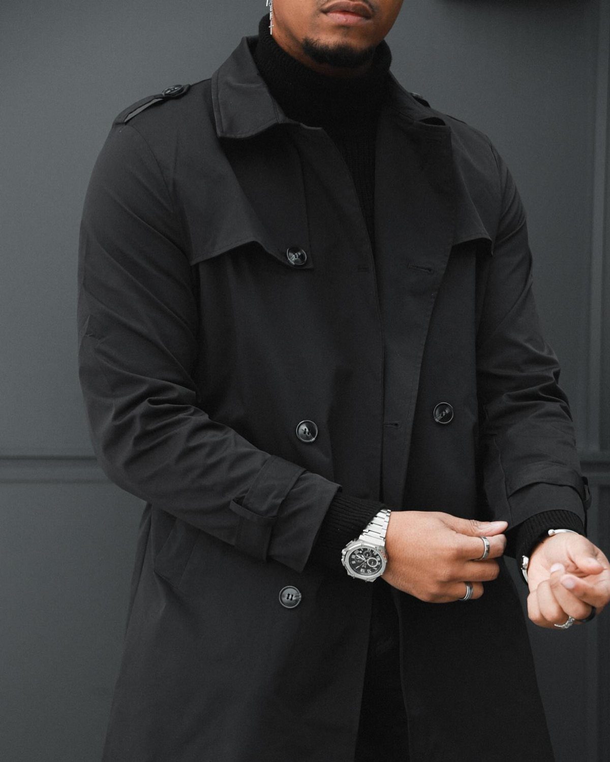 Man wearing a black turtleneck and black trench coat with silver accessories.