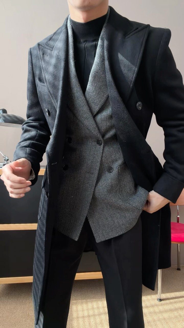 Man wearing a black turtleneck under a grey waistcoat and black overcoat.