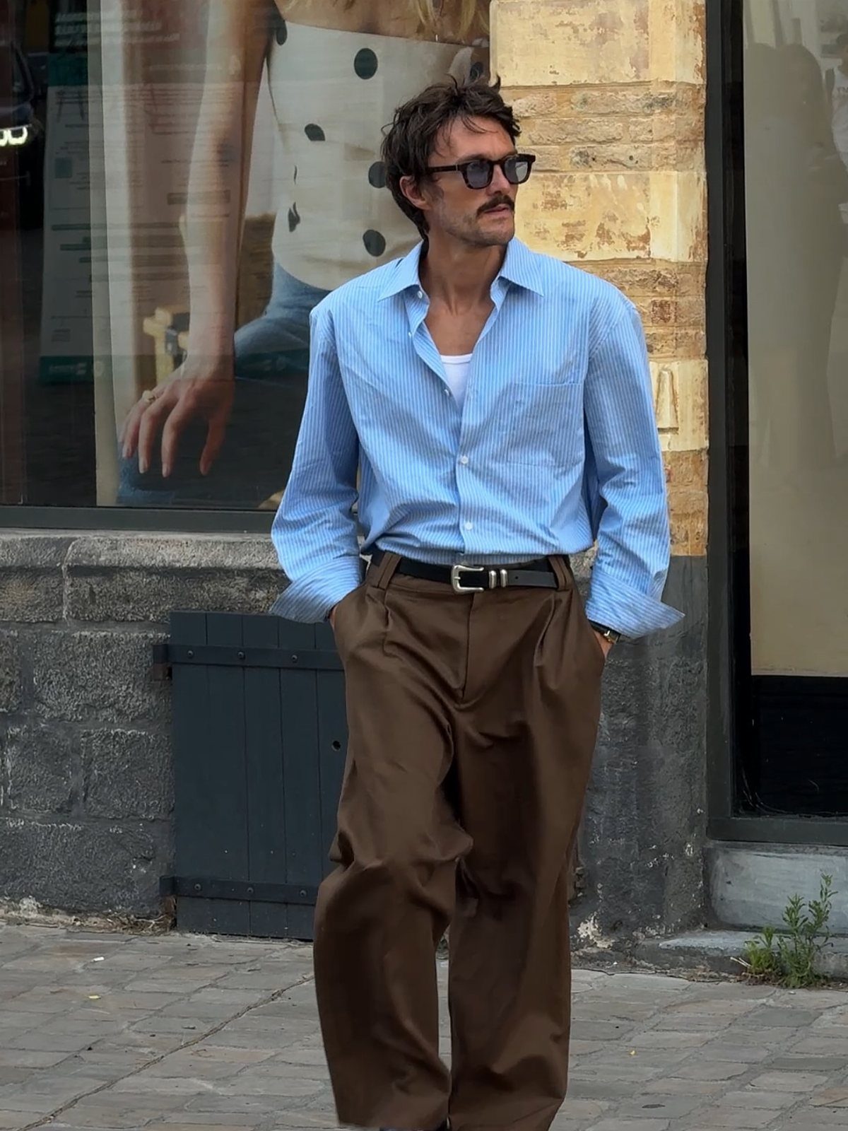Man wearing a light blue striped shirt and wide-leg brown trousers on a street