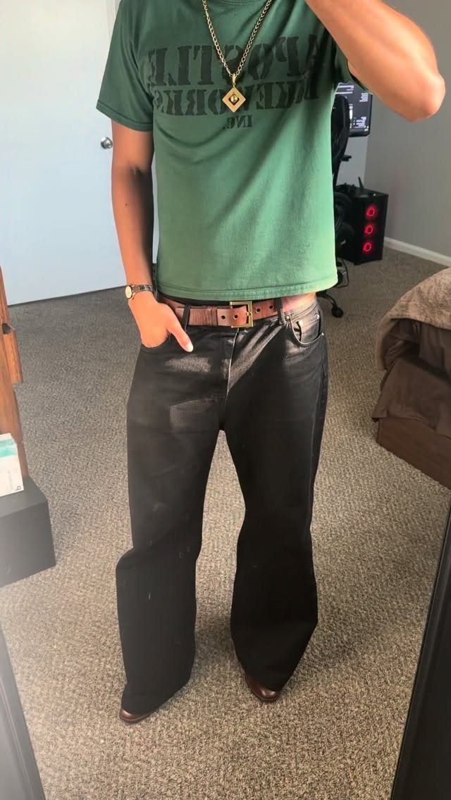 Person wearing a green t-shirt and black bootcut jeans standing on grey carpet