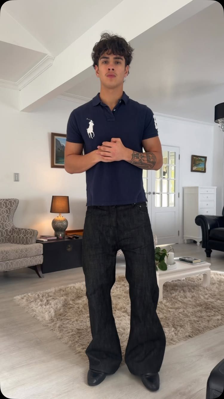 Man wearing a navy polo shirt and dark bootcut jeans in a living room