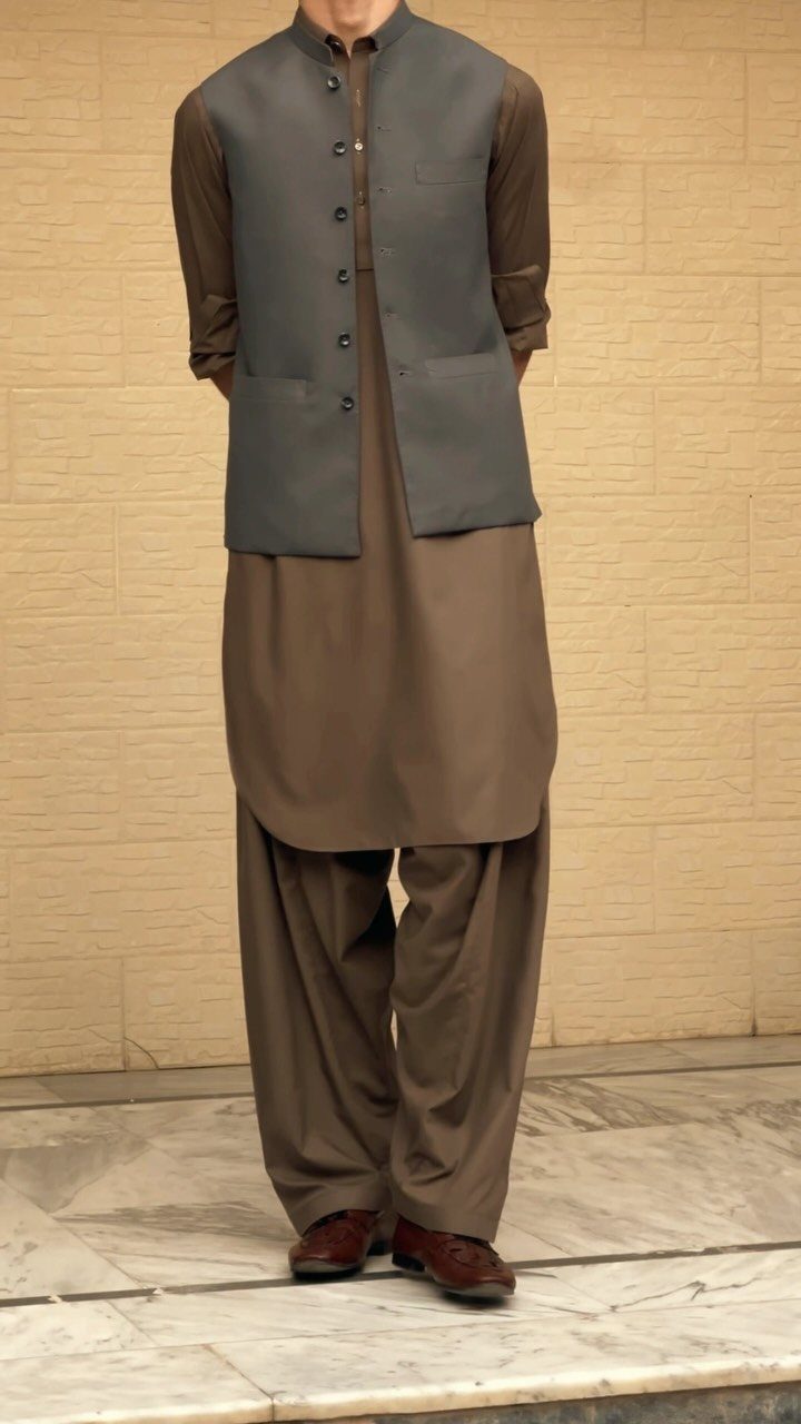 Man wearing a brown shalwar kameez with a grey waistcoat and brown shoes.