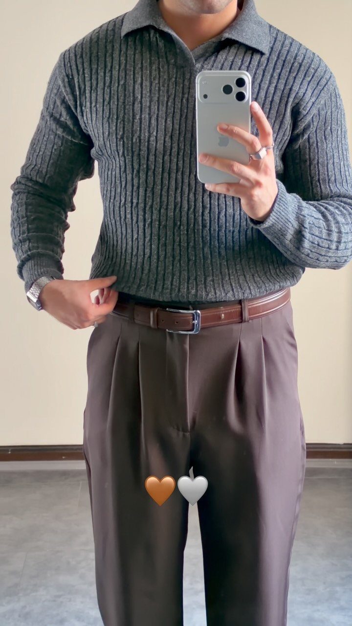 Man wearing a grey ribbed polo shirt and brown pleated trousers with belt.
