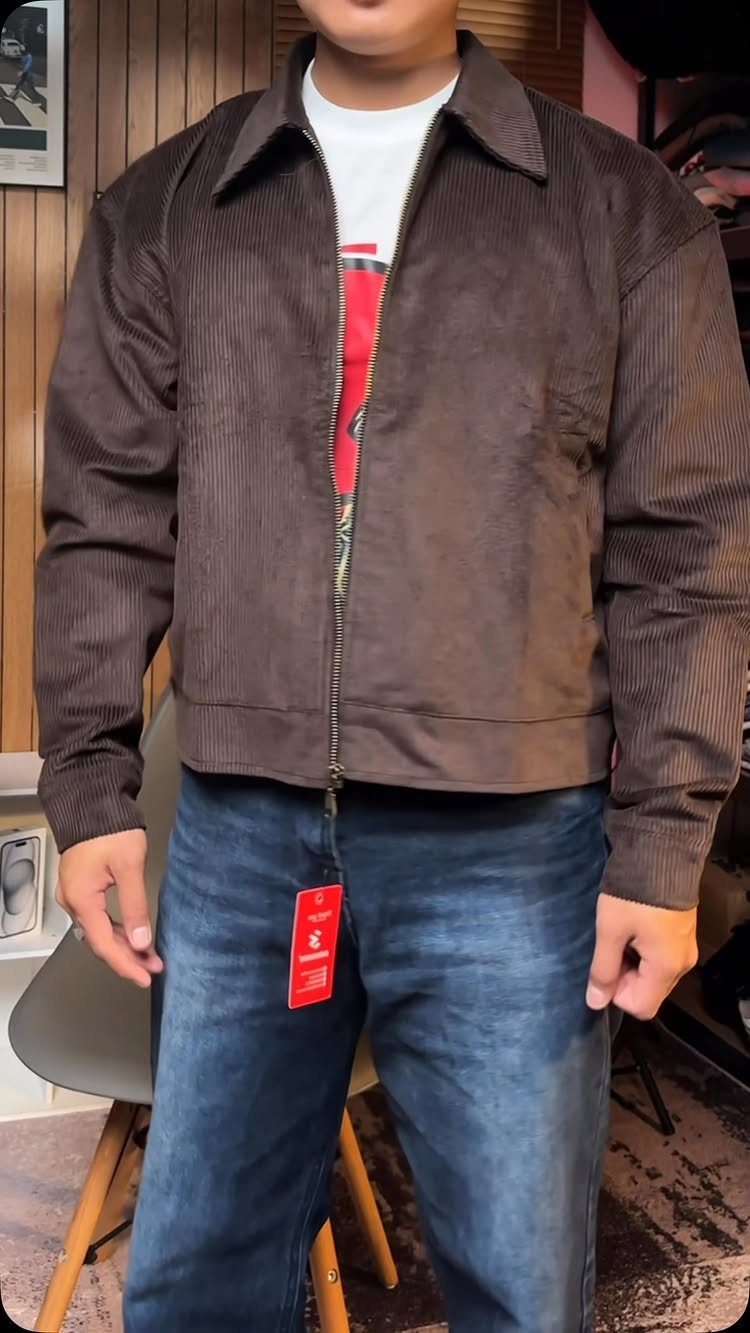 Man wearing a brown corduroy jacket, white t-shirt, and blue denim jeans.