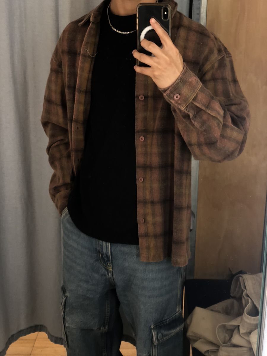 Man wearing a brown plaid flannel overshirt over a black shirt and blue jeans.
