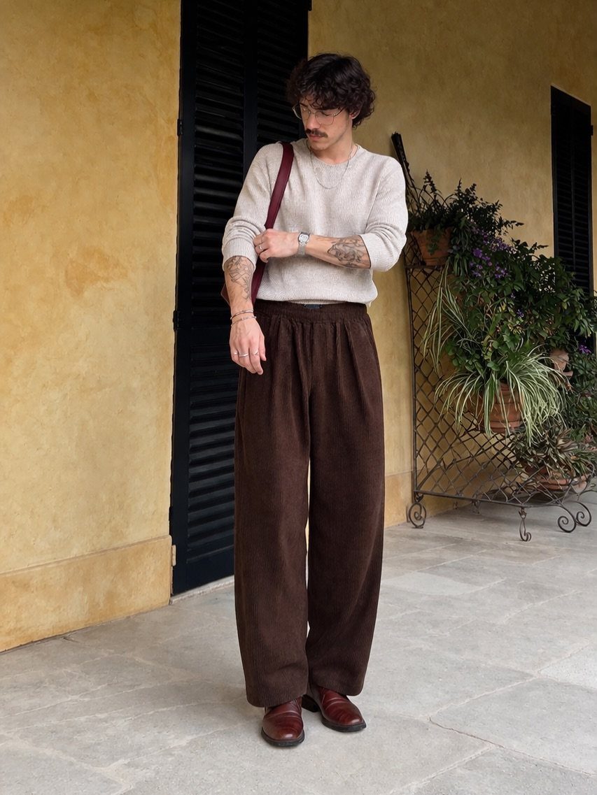 Man wearing wide-leg brown corduroy trousers and a cream sweater standing outdoors.