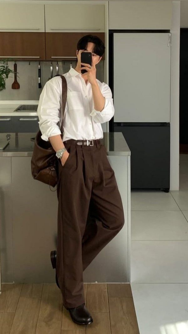 Man in white shirt and wide-leg brown trousers posing for a mirror selfie.