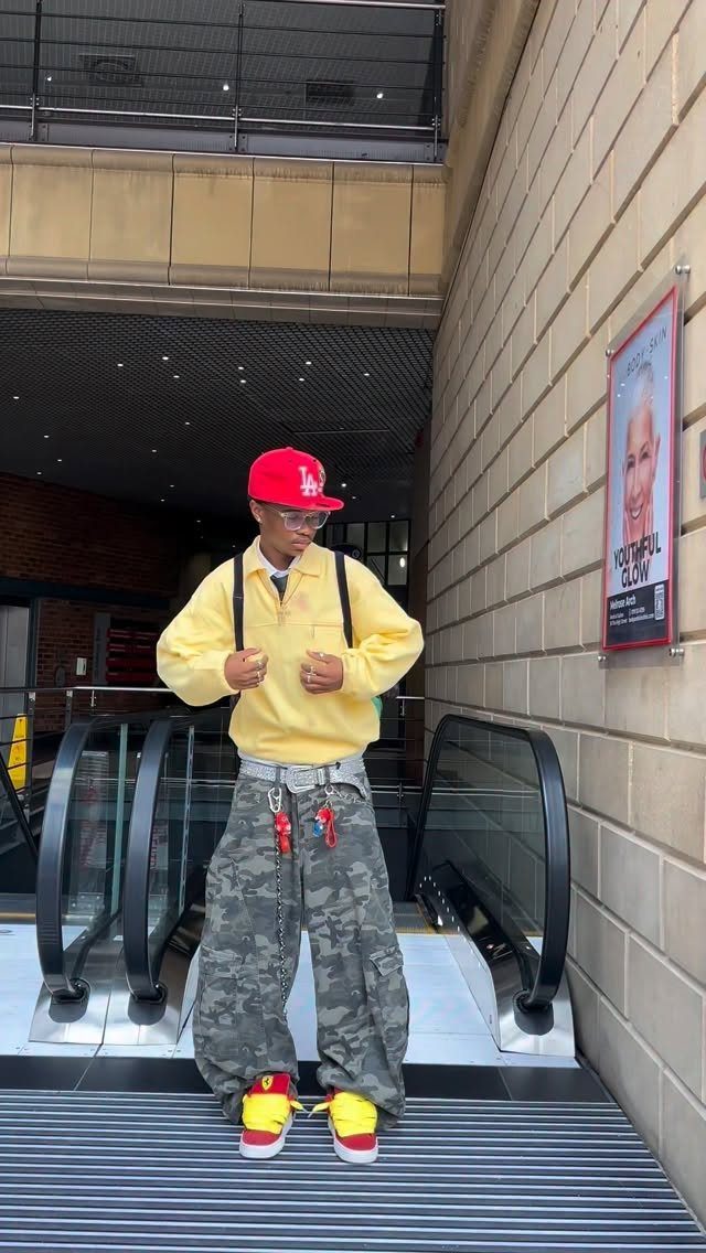 Person wearing a yellow shirt, oversized grey camo pants, and a red cap.
