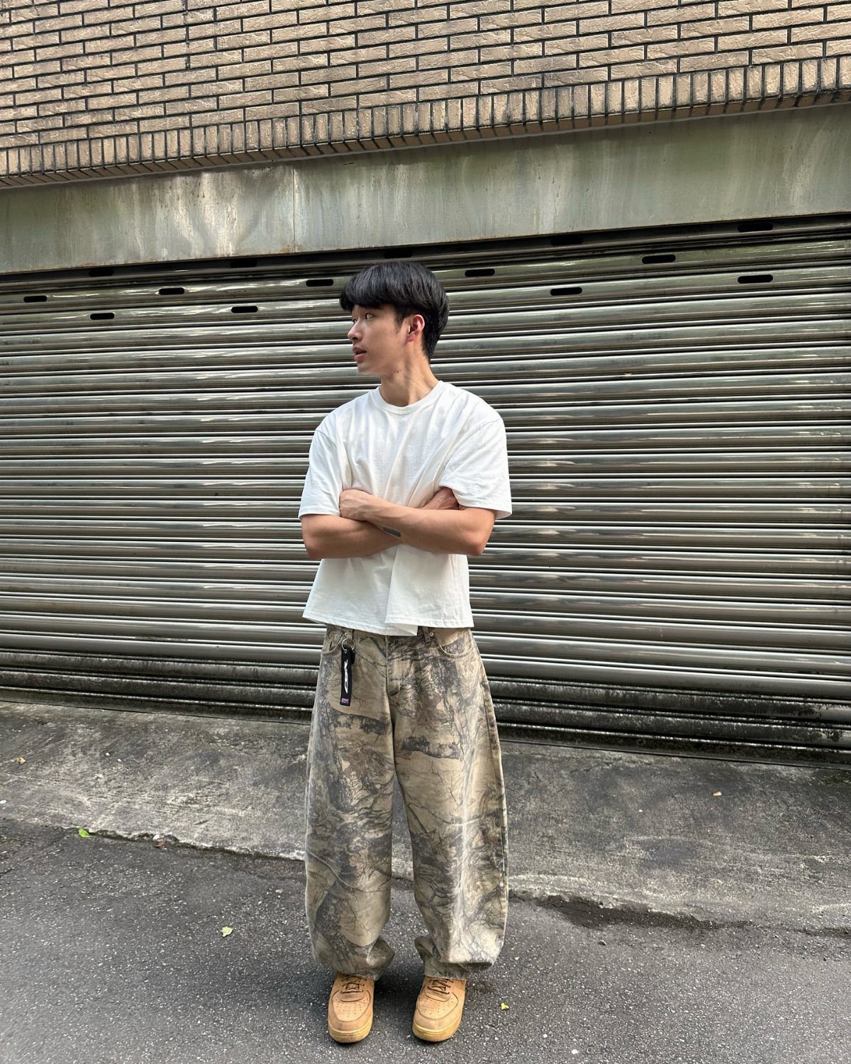 Man wearing an oversized white t-shirt and loose camouflage pants with tan shoes.