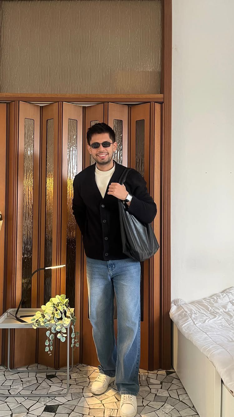 Man in black cardigan and light blue jeans posing in a modern room