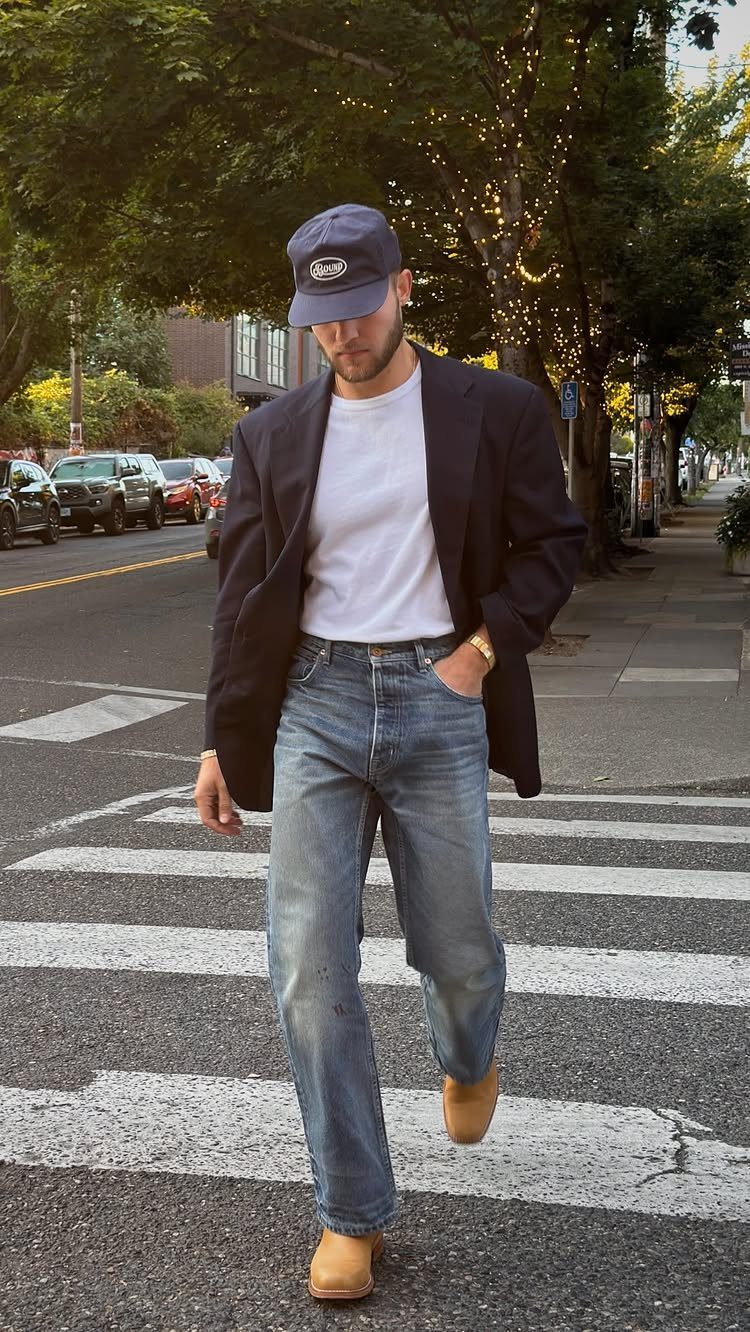 Man in navy blazer and blue jeans walking across a city street crosswalk