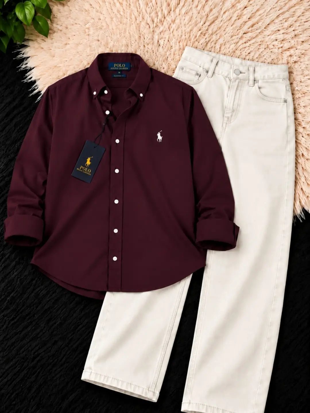 Maroon button-down shirt and off-white trousers laid flat on a textured background.
