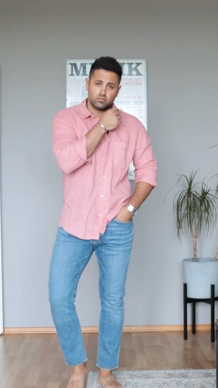 Man in pink button-down shirt and light blue jeans posing indoors.