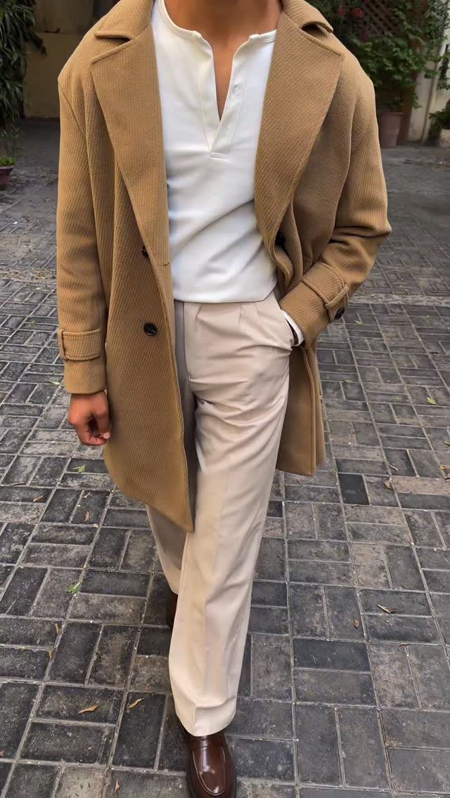 Man in tan overcoat, white shirt, and beige trousers on cobblestone street.