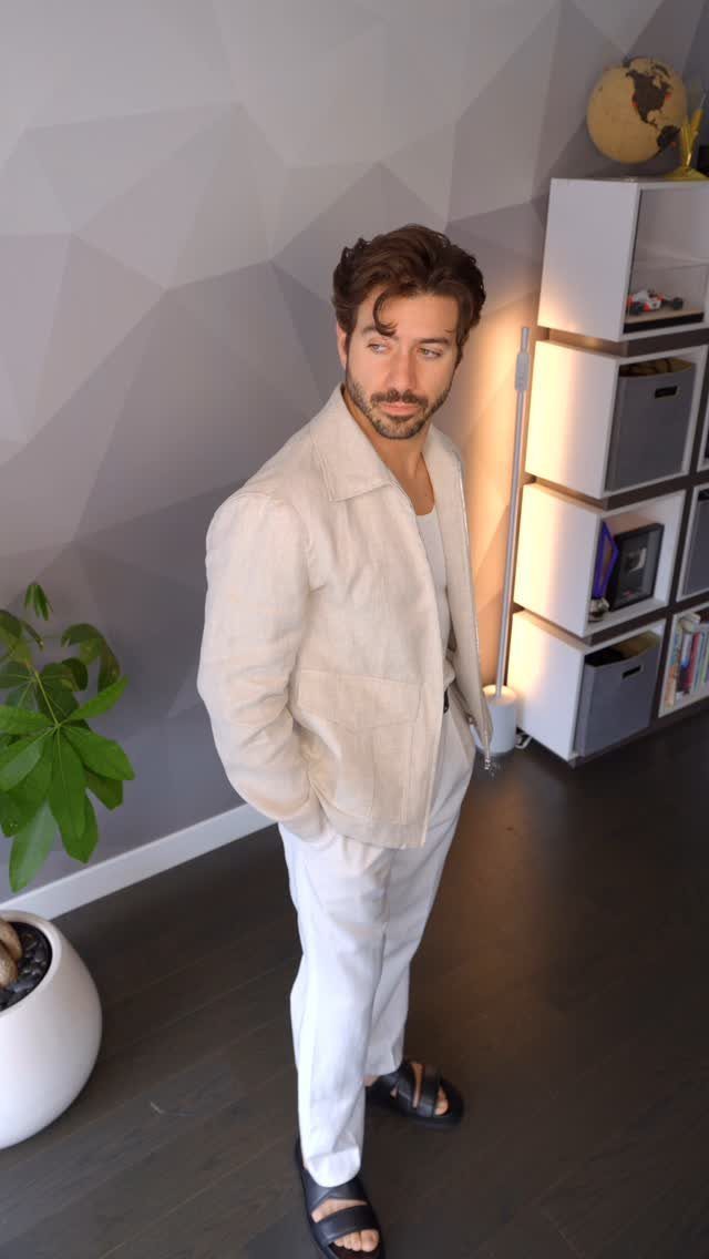 Man wearing a beige linen jacket and white trousers in a modern room.
