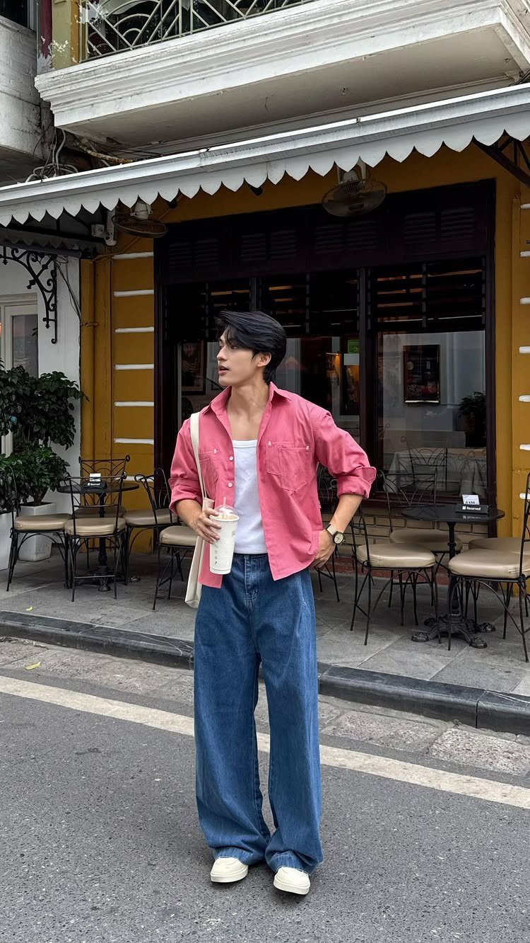 Man in pink open shirt and wide-leg blue jeans standing on city street