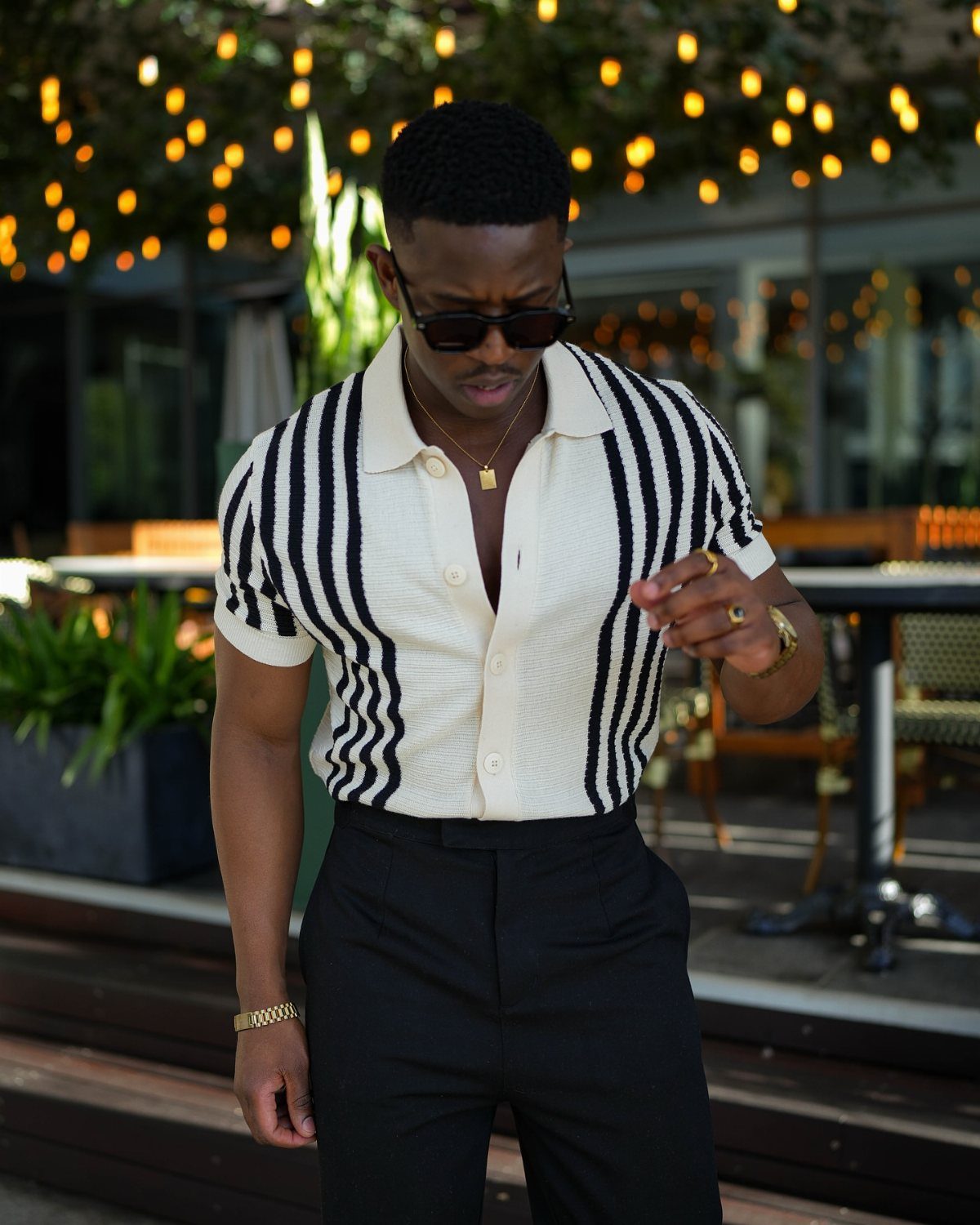 Man wearing a striped white polo shirt and black trousers in an outdoor setting