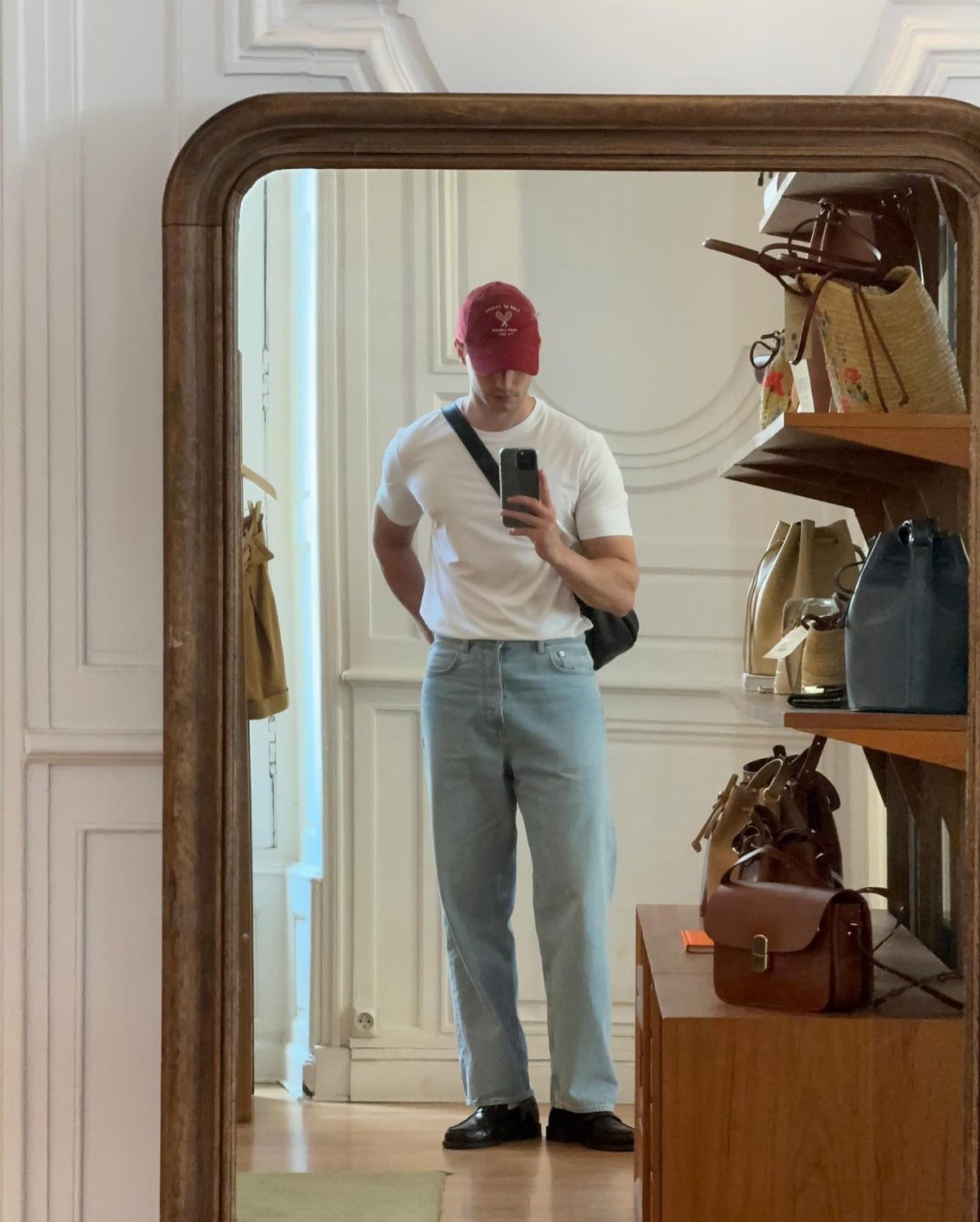 Man in light blue jeans, white t-shirt, and black loafers taking a mirror selfie.